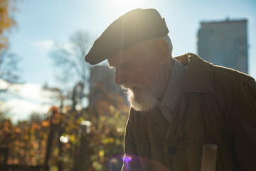 Portrait of old man in garden. Old man on street. Black cap on head of old man.