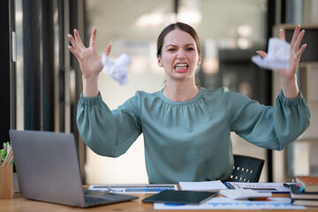 Aggressive businesswoman at her desk throwing crumpled paper balls.