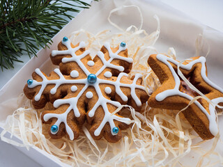 Christmas gingerbread cookies lie in a white box with straw near a pine branch. christmas cookies with icing. cookie in the form of a snowflake with blue dots. gingerbread lies on a white table.