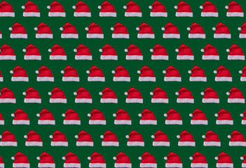 Repeating christmas pattern of santa claus hats on green background, festive pattern, new year concept.