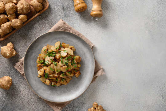 Fresh roasted Jerusalem artichoke root, sunchokes with garlic and parsley on gray background. View from above. Copy space.