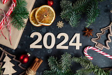 On the table is a gift surrounded by Christmas tree branches, wooden toys, spices and numbers 2024