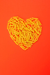 Obraz na płótnie Canvas Macaroni uncooked short dry pasta heart shaped layout. Valentine's day symbol, valentine on red background. Love cooking and food concept
