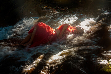 Asian woman in red dress sleeping in hill waterfall at evening