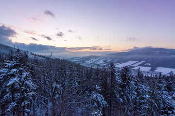 View of snow-covered trees and mountains at sunset from the viewpoint of Certovy kameny in Jeseniky mountains in Czech republic.