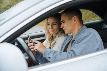 A young couple on a road trip looking at a map on their phone in a navigator.