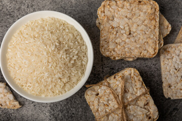 Rice cakes on a black texture table, against the background of a plate of rice. Close-up. Healthy food. Diet food.