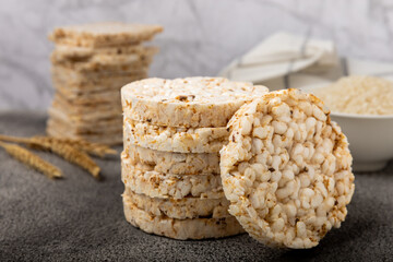 Rice cakes on a black texture table, against the background of a plate of rice. Close-up. Healthy food. Diet food.