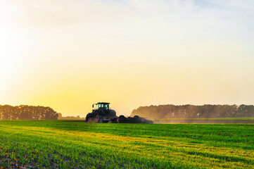 the tractor plows the ground in the spring in the field before planting the grain. Morning dawn in the field. High quality photo