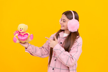 Happy girl child smile pointing finger at teddy bear yellow background, valentines gift