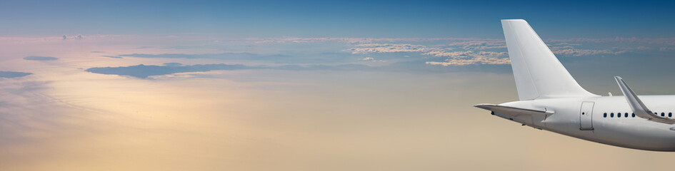 Obraz premium Passenger airplane at cloudy sky background in pastel colors with copy space. Wide landscape over the sea with an aircraft in sunrise beams for your travel concept of air trip or transportation.