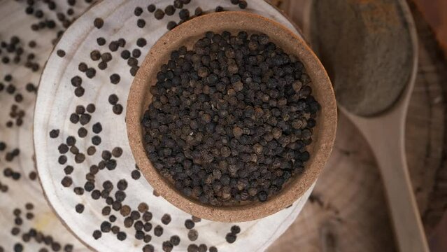  Black peppercorns. In the background a wooden spoon with black pepper powder.