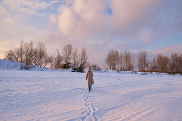 Naklejka na ściany i meble A young woman walks in the snow on a sunny frosty day, enjoying winter moments and nature, wearing winter clothes. Winter time concept, walk