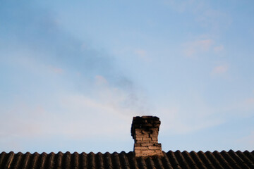 Defocus smoke from the chimney of a house fueled with coal. Black smoke from the chimney of an apartment building during heating and heating on the roof of slate. Carbon monoxide. Out of focus