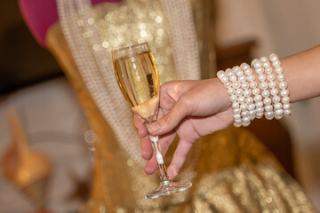 main de jeune femme avec des bracelets de perles de culture tenant une flute de champagne
