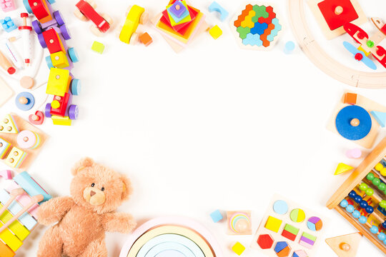 Baby kids toys frame background. Teddy bear, wooden educational, musical, sensory, sorting and stacking toys, wooden train, rainbow, colorful building blocks on white background. Top view, flat lay