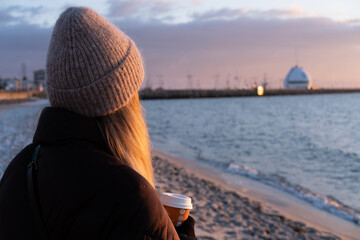 People drink cup of coffee during sunset on the beach in winter blurred