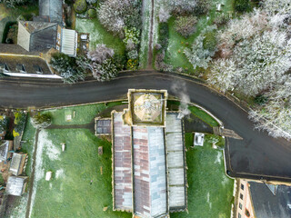 Drone view of a typical English church showing its spire and roof structure. Seen within a rural village.