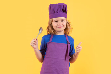Funny kid chef cook with spoon, studio portrait. Kid in cooker uniform and chef hat preparing food on studio color background. Cooking, culinary and kids food concept.