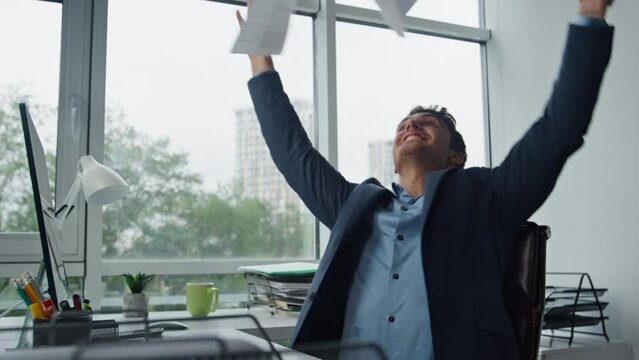 Smiling businessman throwing papers at glass workplace. Happy manager celebrate