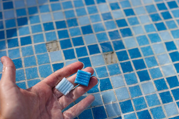 Hand holding small tile from floor of swimming pool. Damaged swimming pool.