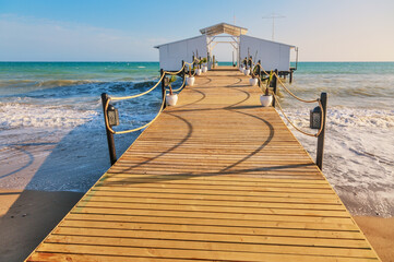 Obraz premium Wooden sea pier in sun lights at the sandy beach