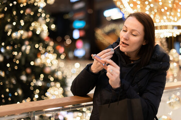 Woman paints her lips on a background with Christmas tree lights bokeh