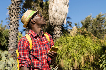 African man with hat and cell phone visiting a botanical garden in Barcelona (Spain).