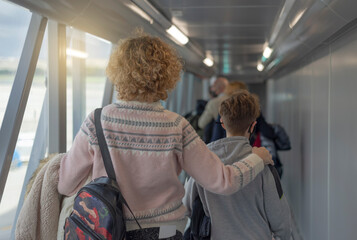 A woman hugs her teenage son as he enters the boarding tunnel of an airplane.