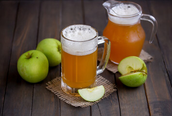 Traditional russian drink apple kvass. Glass of homemade sparkling apple cider with fresh apples and pitcher on wooden background. Selective focus.