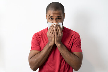 photo of young dark-skinned, sick, student, worker patient with allergy, cold blowing his nose,...
