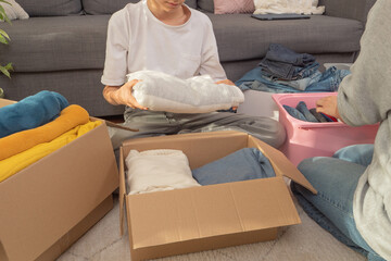 Woman and son sorting clothes and packing into cardboard box. Donations for charity, help low...