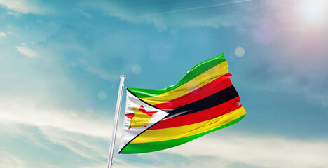 Waving Flag of Zimbabwe in Blue Sky. The symbol of the state on wavy cotton fabric.