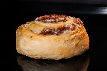 Baked cinnamon bun on tray in electric oven - close up view, black background. Swedish cuisine, homemade bakery, food, cooking and pastry concept