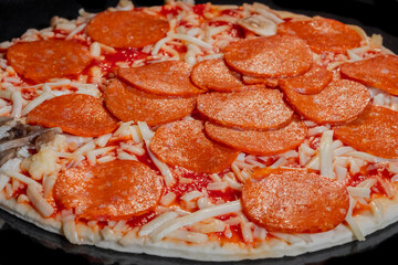 Close up: uncooked pizza with pepperoni, cheese, sause on tray in electric oven. Italian cuisine, homemade bakery, fast food, cooking, semi-finished products and raw concept