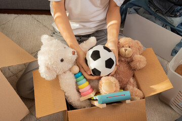 Teenager sorting and collect kid toys, clothes into boxes at home. Donations for charity, help low income families, declutter home, sell online, moving into new home, recycling, sustainable living - obrazy, fototapety, plakaty