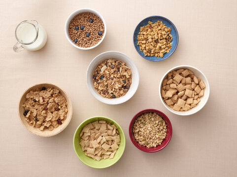 Overhead view of bowls of a variety of healthy cereals and jug of milk, studio shot