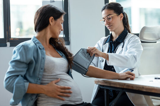 Female gynecologist checking the blood pressure of her pregnant patient in the clinic. - Powered by Adobe