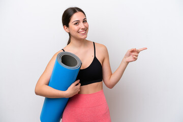 Young sport girl going to yoga classes while holding a mat isolated on white background pointing finger to the side