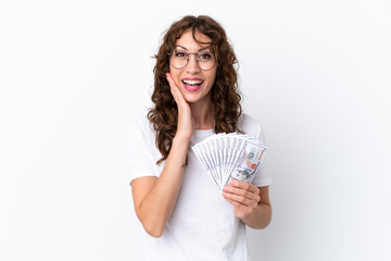 Young woman with curly hair taking a lot of money isolated background on white background with surprise and shocked facial expression