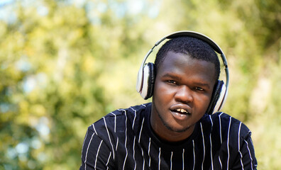 African man concentrated with music headphones looking at camera in a park. Digital nomad
