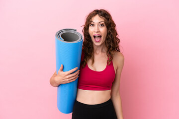 Young sport woman going to yoga classes while holding a mat isolated on pink background with...