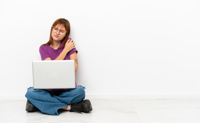 redhead girl with a laptop sitting on the floor suffering from pain in shoulder for having made an effort