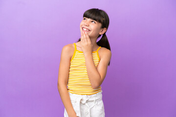 Little caucasian kid isolated on purple background looking up while smiling