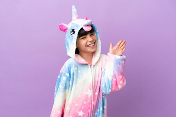 Little kid wearing a unicorn pajama isolated on purple background saluting with hand with happy expression