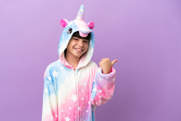 Little kid wearing a unicorn pajama isolated on purple background pointing to the side to present a product