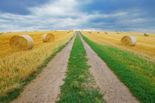 Field road through stubble field with straw rolls and rain clouds, Hesse, Germany, Europe