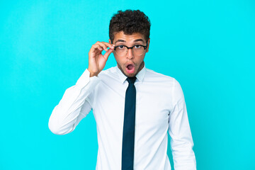 Young business Brazilian man isolated on blue background with glasses and surprised