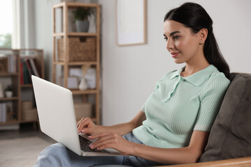 Young woman working with laptop in armchair at home