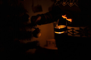 Ukraine, winter 2022. A woman decorates a Christmas tree in the dark with a candle.
